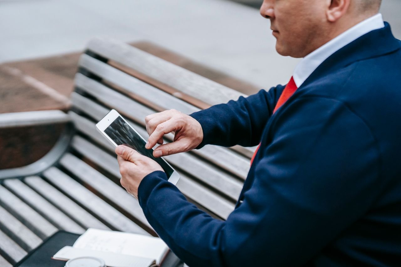 A professional man in a suit uses a tablet outdoors, showcasing modern technology in a casual setting.
