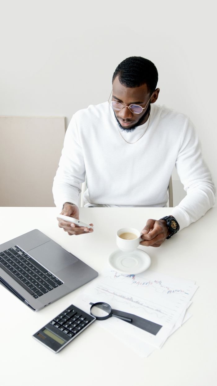 A professional man multitasking with a smartphone and coffee in an office setting.